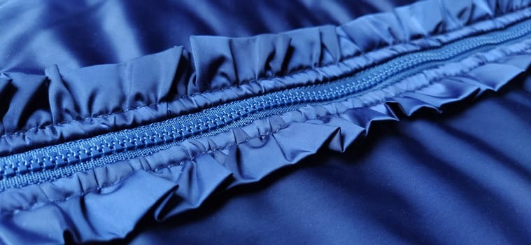 Buttoned zip on a blue raincoat. Waves and folds in the fabric. Beautiful flounces, ruffles, frills. Decorative finishing of a garment. Smocked, sewn silk fabric. Nice casual wear