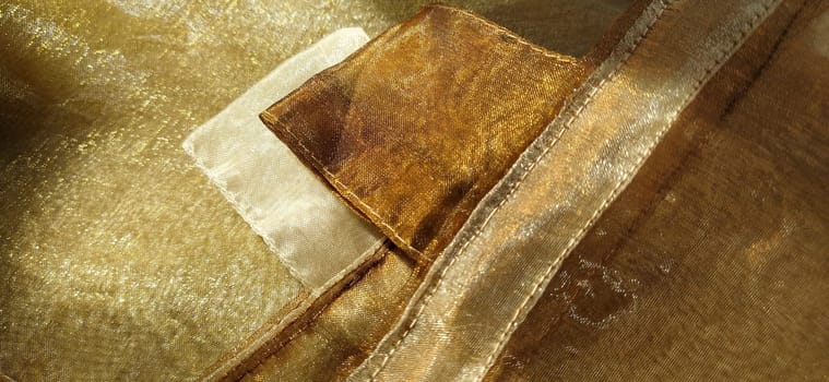Curtain loops. Beautiful gold fabric. Organza in yellow, orange, beige and brown shades. Pleats in the fabric. Shiny gradient under the light. Folded silky tulle. Transparent curtain material.
