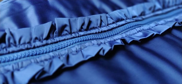 Buttoned zip on a blue raincoat. Waves and folds in the fabric. Beautiful flounces, ruffles, frills. Decorative finishing of a garment. Smocked, sewn silk fabric. Nice casual wear