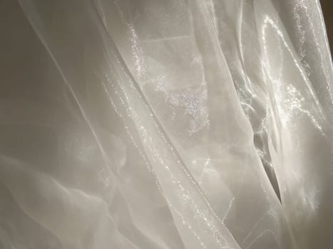 Organza in white and beige or champagne color close-up. Lightweight sheer tulle curtains under side lighting.
