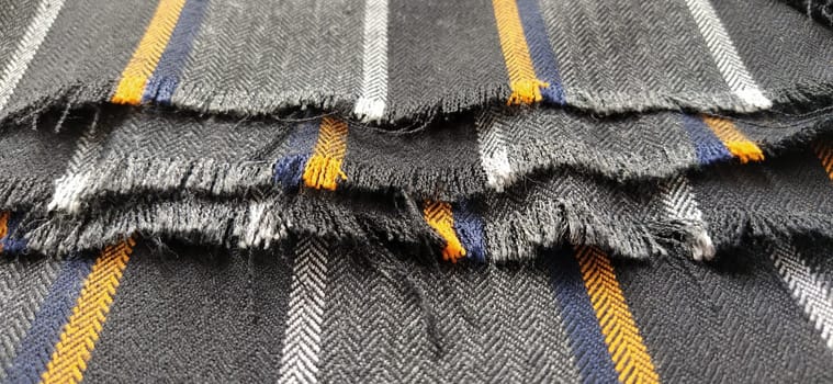 Gray-black fabric with orange and blue stripes. Textile fabric folded neatly on the surface. Natural wool material for sewing clothes and upholstery. Lifestyle. Close-up. Soft focus.