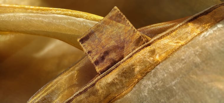Curtain loops. Beautiful gold fabric. Organza in yellow, orange, beige and brown shades. Pleats in the fabric. Shiny gradient under the light. Folded silky tulle. Transparent curtain material.