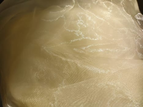 Organza in white and beige or champagne color close-up. Lightweight sheer tulle curtains under side lighting.