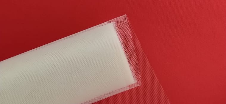 Fabric - white mesh in a roll on a red background. Nylon tape for tying bows on hair. A skein of tulle fabric. Copy space.