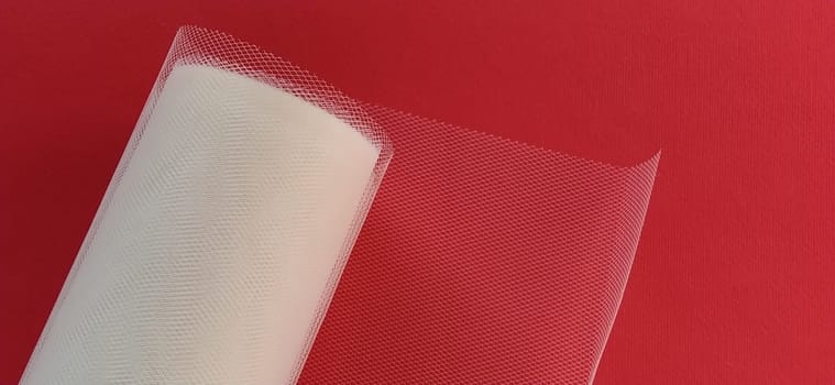 Fabric - white mesh in a roll on a red background. Nylon tape for tying bows on hair. A skein of tulle fabric. Copy space.