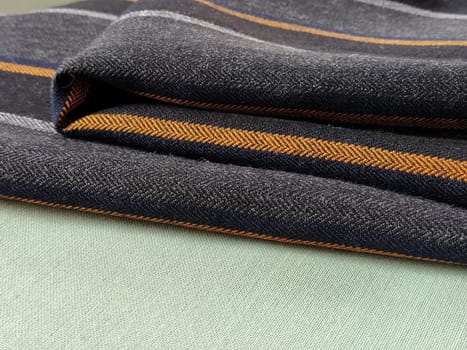 Light green and black-gray folded fabric with orange and dark blue stripes. Interior decoration. Dress fabrics in casual style. Dense material for indoor curtains and furniture finishing.