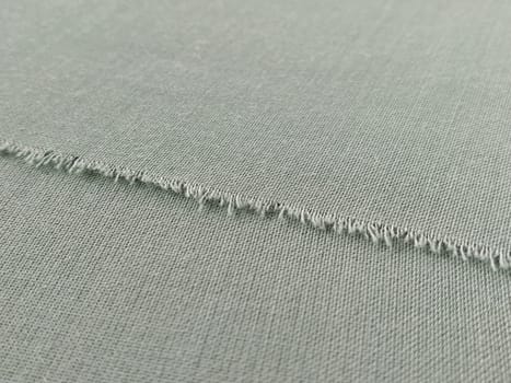 Ripped edge of fine woolen fabric in green or blue. Loose threads at the edge of a piece of textile. Close-up. Woven background. Calm green pastel color.