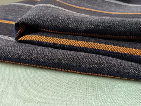Gray-black fabric with orange and blue stripes. Textile fabric folded neatly on the surface. Natural wool material for sewing clothes and upholstery. Lifestyle. Close-up. Soft focus.