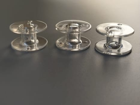 Three transparent plastic sewing machine bobbins. Textile industry. Detail of sewing equipment. Gray background, back lighting.
