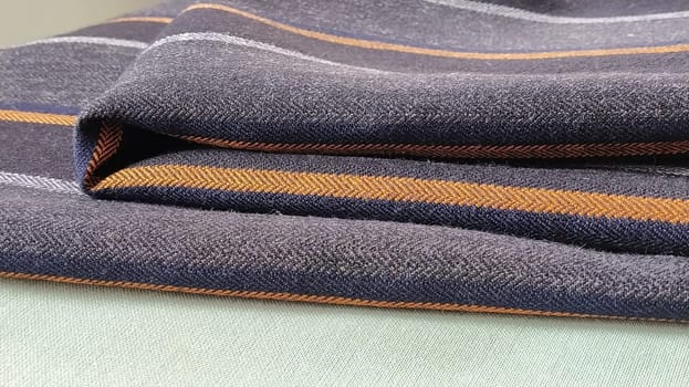 Gray-black fabric with orange and blue stripes. Textile fabric folded neatly on the surface. Natural wool material for sewing clothes and upholstery. Lifestyle. Close-up. Soft focus.