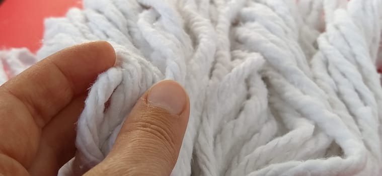 A woman's hand touches the cotton threads of the mop head. Choosing a mop for cleaning. Household cleaning work. White ropes. Cleaning lady's fingers