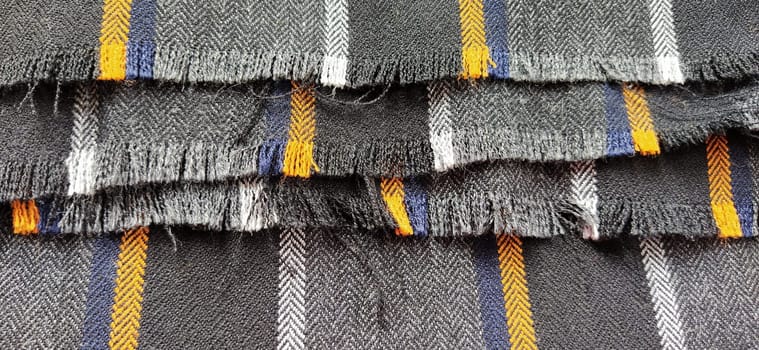 Light black-gray folded fabric with orange and dark blue stripes. Ripped, unfinished fabric edge. Interior decoration. Dress fabrics in casual style. Dense material for furniture finishing.