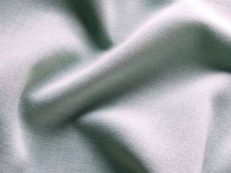 Beautifully folded light green fabric. Soft pleasant waves and flounces on textiles. Close-up. Drapery for curtains, fabric for dressmaking or upholstery.