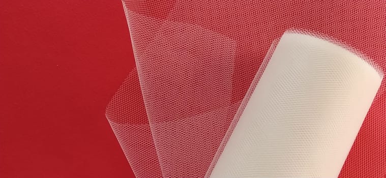 Fabric - white mesh in a roll on a red background. Nylon tape for tying bows on hair. A skein of tulle fabric. Copy space.