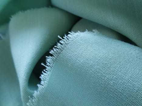 Close up of a woolen fabric of green color. Abstract canvas background, empty template. Thin natural fabric, wool or linen. The edge of the fabric is treated against chapping.