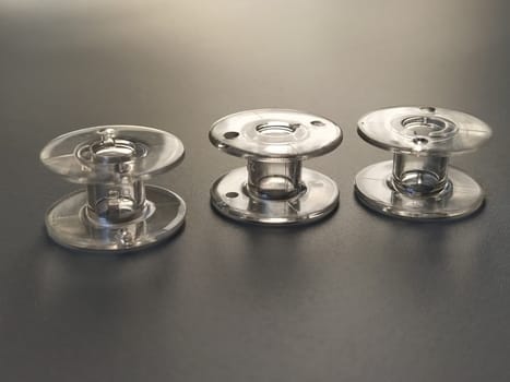 Three transparent plastic sewing machine bobbins. Textile industry. Detail of sewing equipment. Gray background, back lighting.
