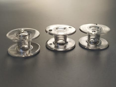 Three transparent plastic sewing machine bobbins. Textile industry. Detail of sewing equipment. Gray background, back lighting.