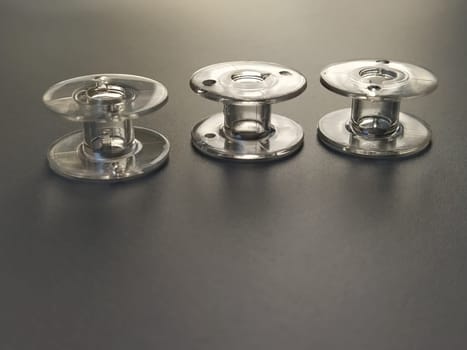 Three transparent plastic sewing machine bobbins. Textile industry. Detail of sewing equipment. Gray background, back lighting.