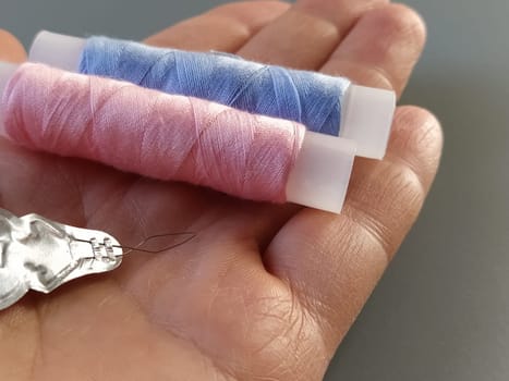 device for drawing the thread into the eye of the needle. Bobbins with blue and pink threads in the background. A woman holds a needle threader in her hand and shows its thin wire eye.