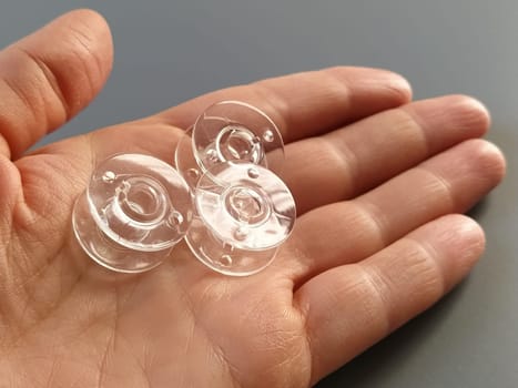 Transparent plastic bobbins from a modern sewing machine in the palm of a woman - a seamstress. Gray background. sewing machines.