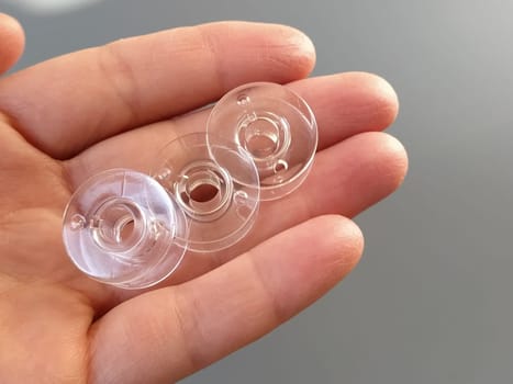 Transparent plastic bobbins from a modern sewing machine in the palm of a woman - a seamstress. Gray background. sewing machines.