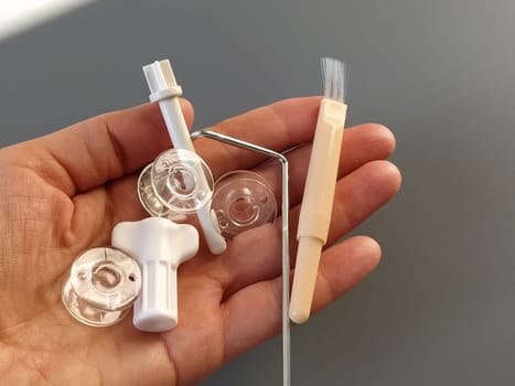 Transparent plastic bobbins from a modern sewing machine in the palm of a woman - seamstresses, needles, thread take-up, whipping tool. Gray background. sewing machines.