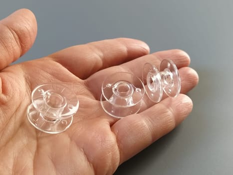Transparent plastic bobbins from a modern sewing machine in the palm of a woman - a seamstress. Gray background. sewing machines.