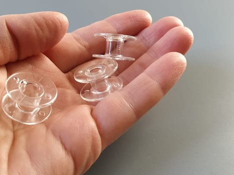 Transparent plastic bobbins from a modern sewing machine in the palm of a woman - a seamstress. Gray background. sewing machines.