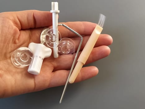 Transparent plastic bobbins from a modern sewing machine in the palm of a woman - seamstresses, needles, thread take-up, whipping tool. Gray background. sewing machines.