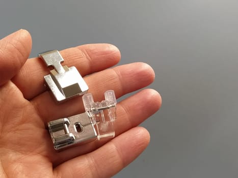 A set of feet for an electric sewing machine in a female hand. Gray backdrop. Metal and plastic objects in the palm of your hand