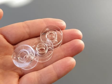 Transparent plastic bobbins from a modern sewing machine in the palm of a woman - a seamstress. Gray background. sewing machines.