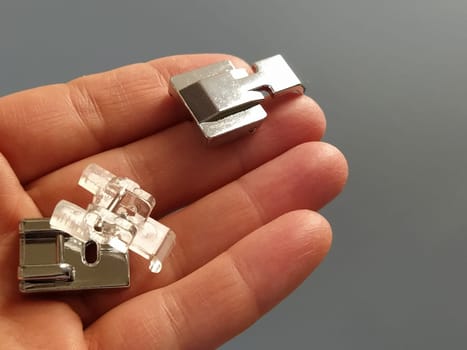A set of feet for an electric sewing machine in a female hand. Gray backdrop. Standard sewing or zigzag foot, for sewing in zippers, overlock foot and for buttons.