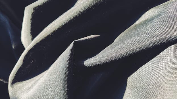 black fabric with interlacing threads close-up. Dark blue tint. Nice beautiful waves on the material. A neatly folded fabric. Interior decoration, sewing clothes and curtains. Textile industry.