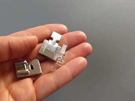 A set of feet for an electric sewing machine in a female hand. Gray backdrop. Standard sewing or zigzag foot, for sewing in zippers, overlock foot and for buttons.