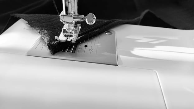 Sewing process on a modern sewing machine, close-up. Sewing machine foot with a needle. Dark blue fabric is trimmed with double wrapping of the fabric edge. Natural sunlight.