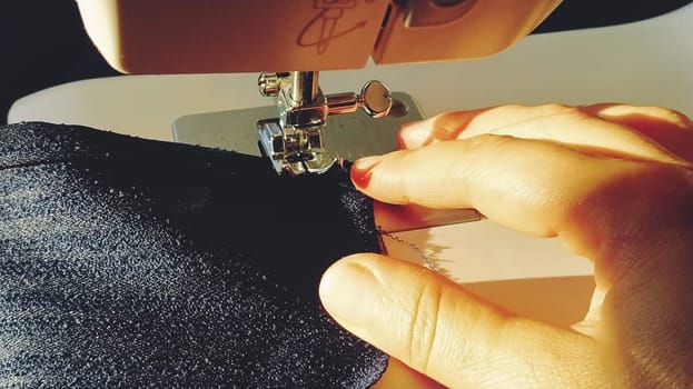 Sewing process on a modern sewing machine, close-up. Sewing machine foot with a needle. Dark blue fabric is trimmed with double wrapping of the fabric edge. Natural sunlight.