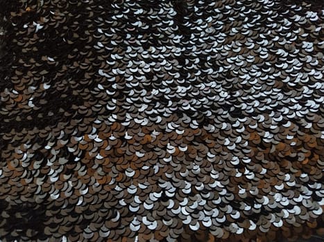 Sequin fabric. Black sequins with white and gray sheen. Reflection of light on individual elements in a chaotic manner. Sewing or Christmas decorative background.