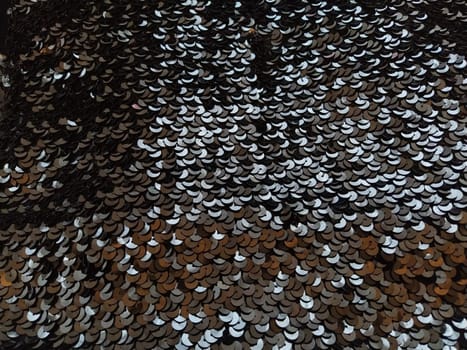 Sequin fabric. Black sequins with white and gray sheen. Reflection of light on individual elements in a chaotic manner. Sewing or Christmas decorative background.