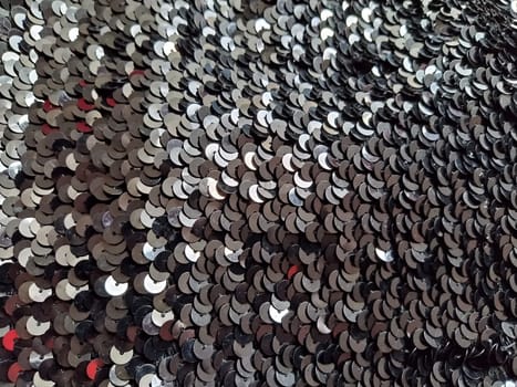 Sequin fabric. Black sequins with white and gray sheen. Reflection of light on individual elements in a chaotic manner. Sewing or Christmas decorative background.