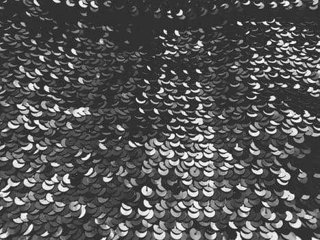 Sequin fabric. Black sequins with white and gray sheen. Reflection of light on individual elements in a chaotic manner. Sewing or Christmas decorative background.