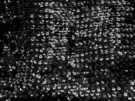 Sequin fabric. Black sequins with white and gray sheen. Reflection of light on individual elements in a chaotic manner. Sewing or Christmas decorative background.