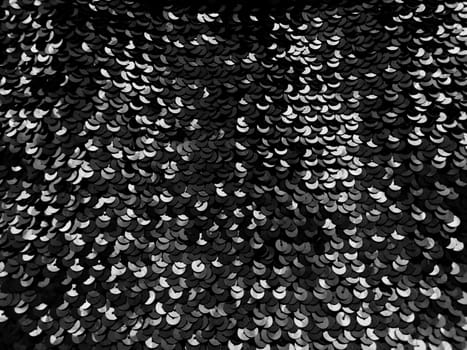Sequin fabric. Black sequins with white and gray sheen. Reflection of light on individual elements in a chaotic manner. Sewing or Christmas decorative background.
