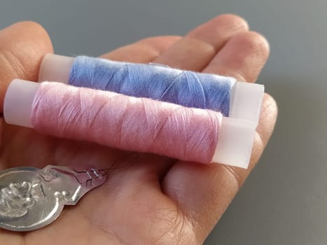 device for drawing the thread into the eye of the needle. Bobbins with blue and pink threads in the background. A woman holds a needle threader in her hand and shows its thin wire eye.
