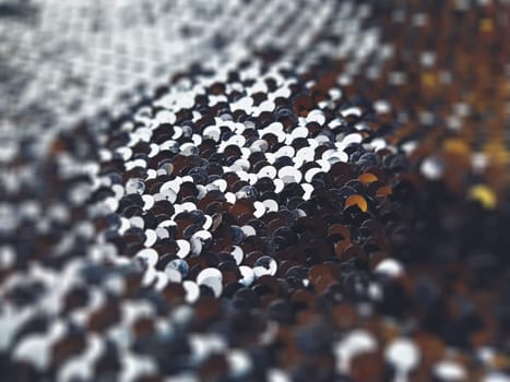 Sequin fabric. Black sequins with white-gray tint. Reflection of light on individual elements in a chaotic manner. Blurred circle background. Soft focus.