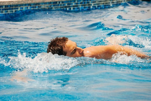 Young man swimmer train swimming in swimming pool. Recreation outdoor water sport.