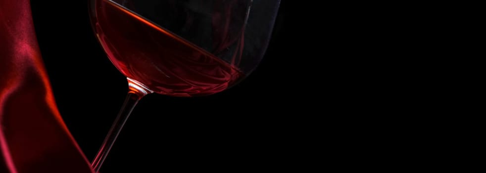 Glass of red wine on red silk against black background. Wine list design layout. Luxury restaurant romantic dinner concept. Closeup wineglass on dark backdrop.