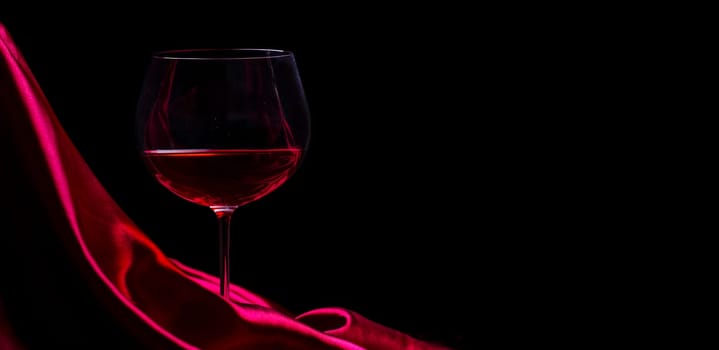 Glass of red wine on red silk against black background. Wine list design background. Luxury restaurant romantic dinner concept.