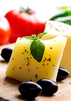 Closeup of goat cheese, olives, fresh tomato, basil and spices on wooden cutting board. Food ingredients for italian pizza recipe. Mediterranean cuisine with dairy product and organic vegetable and herbs.