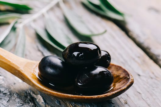 Closeup of fresh black olive in oil on rustic wood table. Organic olive fruit in kitchen wooden spoon. Italian cuisine.