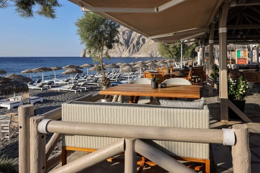 Kamari, Santorini, Greece - July 3, 2021: Sun loungers on the black volcanic beach of Kamari in Santorini. Cyclades, Greece